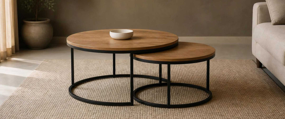 Two round oak-tone nesting tables with black metal frames in a warm neutral living room