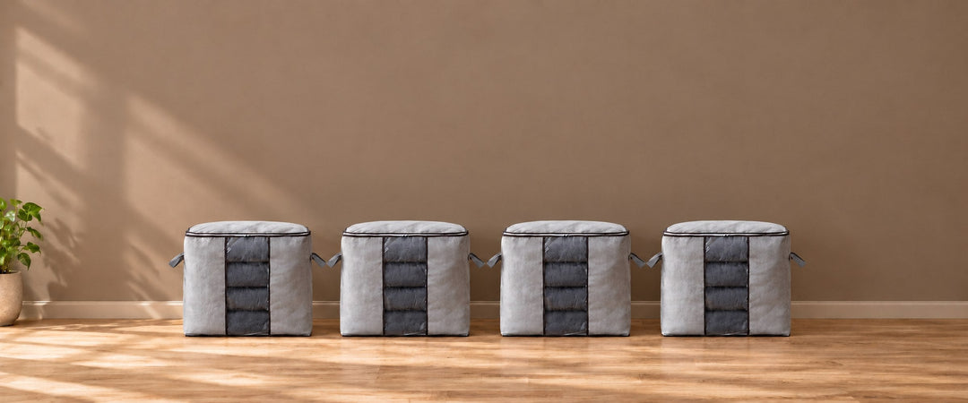 Four grey quilt storage bags with clear front windows showing charcoal blankets in a naturally lit room