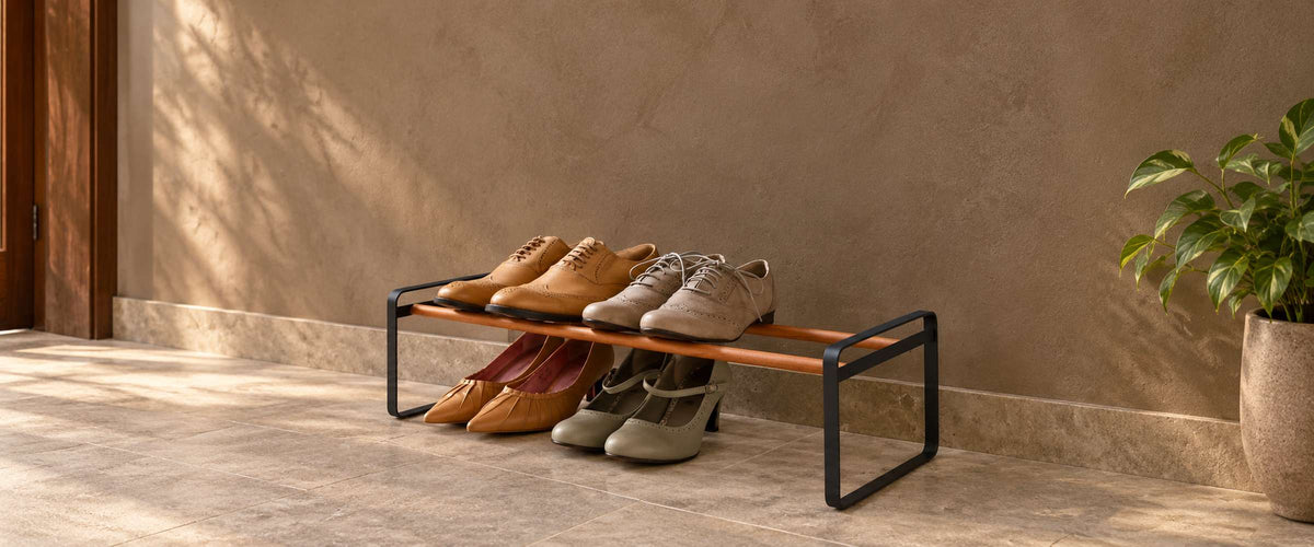 Low black metal shoe rack with wooden rails holding four pairs of shoes in a sunlit entryway