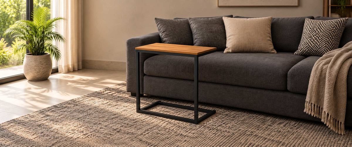 Wood-top iron side table with a black C-shaped frame beside a charcoal sofa