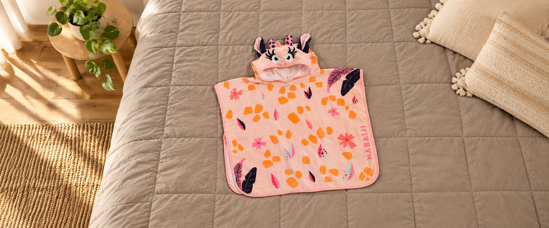 Pink Elunara cow-hood poncho with orange spots and leaf print laid on a warm grey bedspread