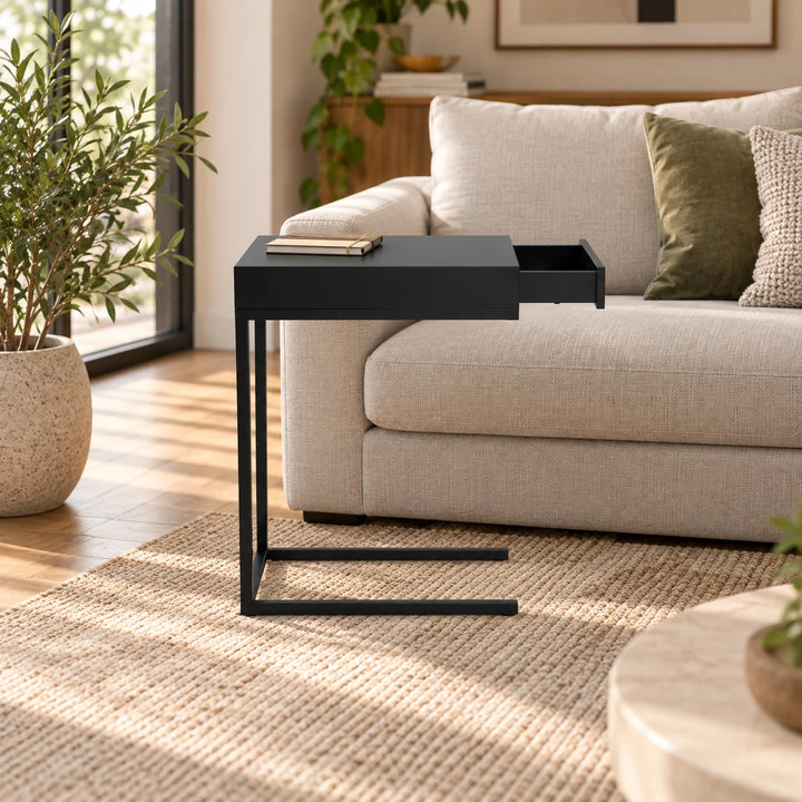 Athow black pull up table with open drawer beside a sofa and natural plant