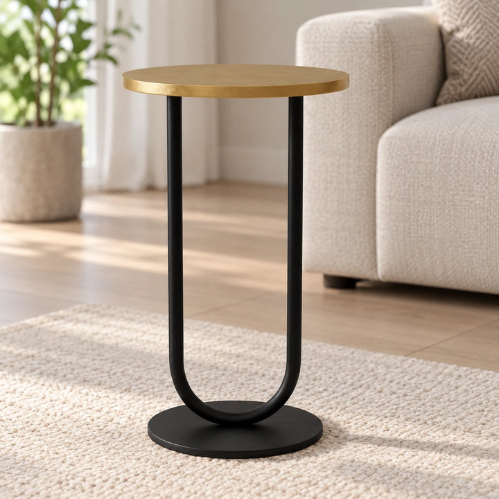 Side table with gold-toned top and black U-shaped support in a daylight room