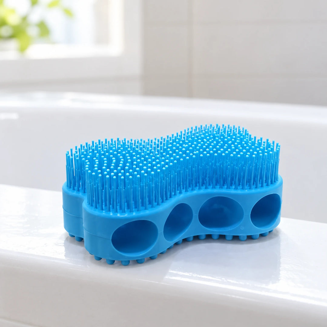 Blue silicone bath brush with four finger holes and soft bristles beside a sunlit bathroom basin