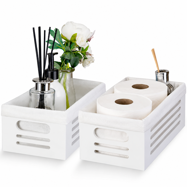 Two white bathroom tissue organizer baskets with fabric liners and cutout handles on a wooden table