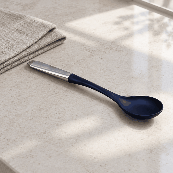 Black silicone spoon with steel handle resting on marble counter beside linen cloth