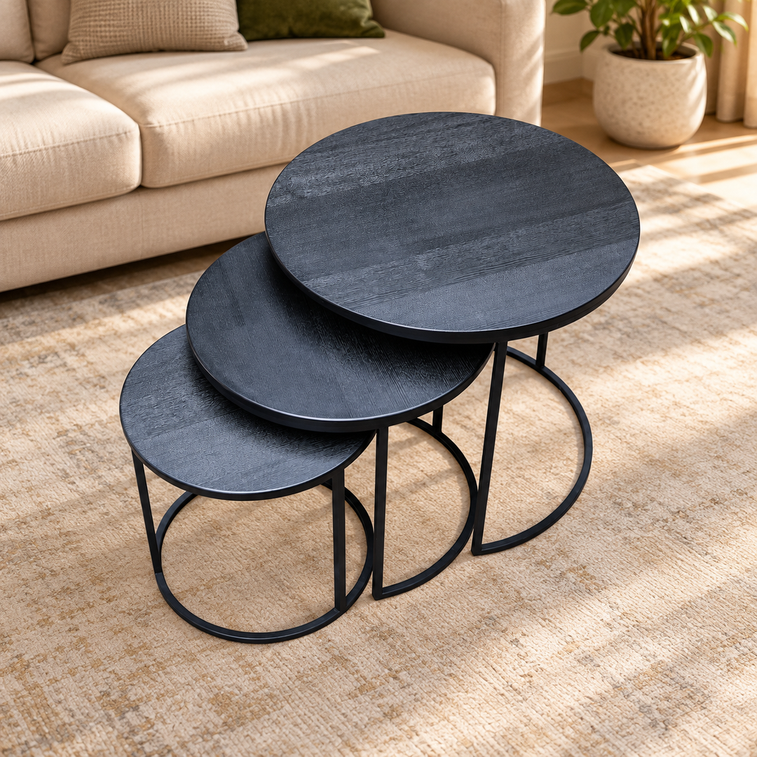 Blackish set of three round nesting tables, shown nested in the original arrangement with dark wood-grain tops and black open metal bases in a warm living room