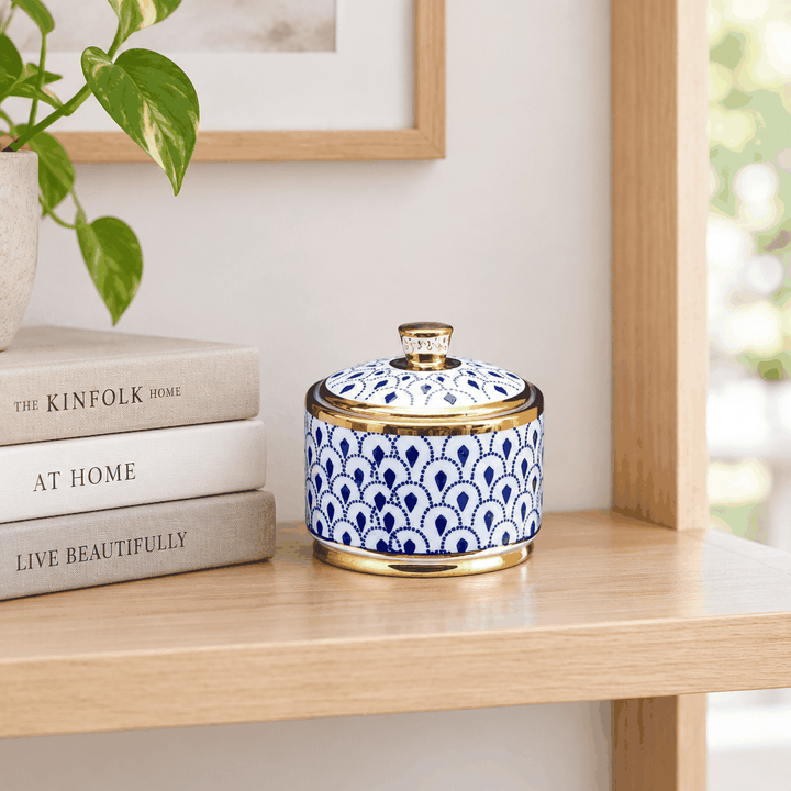 Blue and white patterned ceramic jar with gold lid on wooden shelf beside books