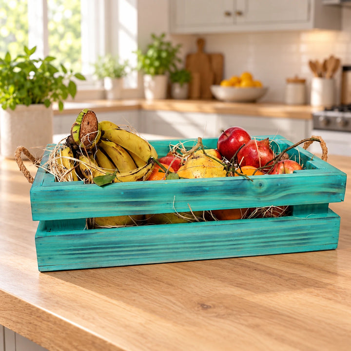 Teal distressed wooden fruit basket with rope handles on a sunlit kitchen island