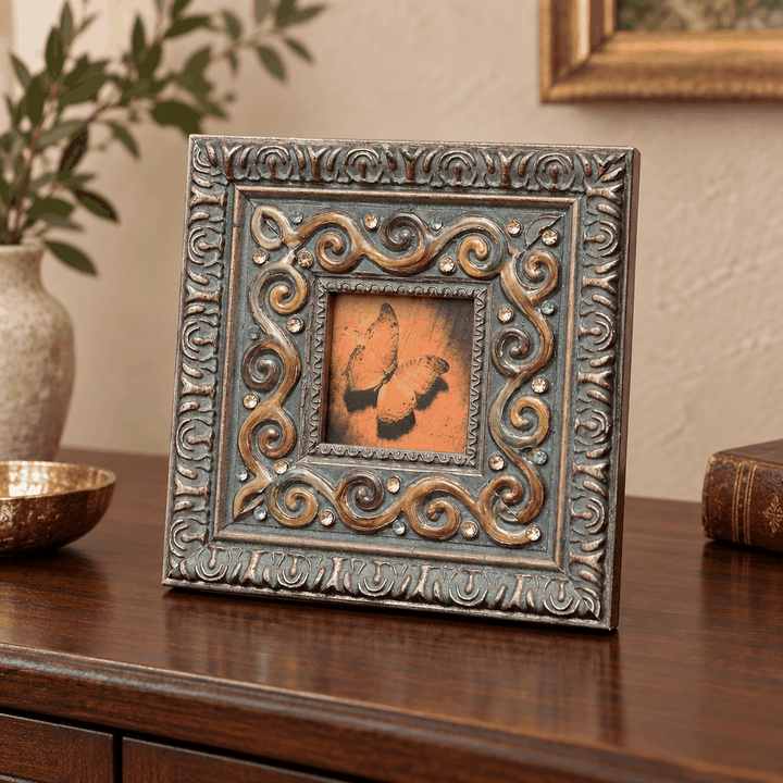 Square antique photo frame with colourful scroll border on wooden sideboard