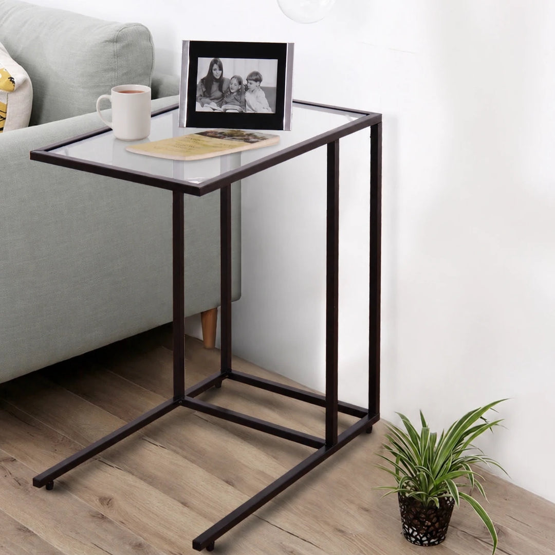 Ceylon slide-under side table with a clear top and dark frame beside a sofa, staged with a mug and book
