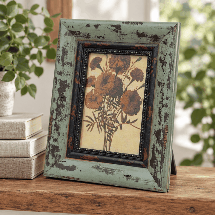 Distressed green photo frame with floral print beside books and plant