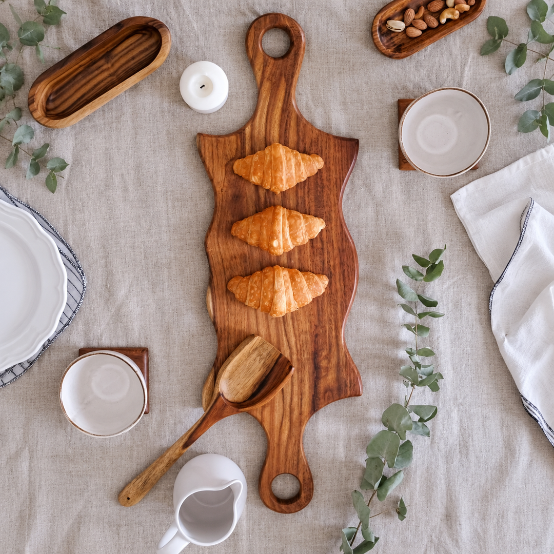 Double swirled wooden platter with handles on white table with herbs