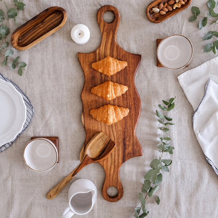 Double swirled wooden platter with handles on white table with herbs