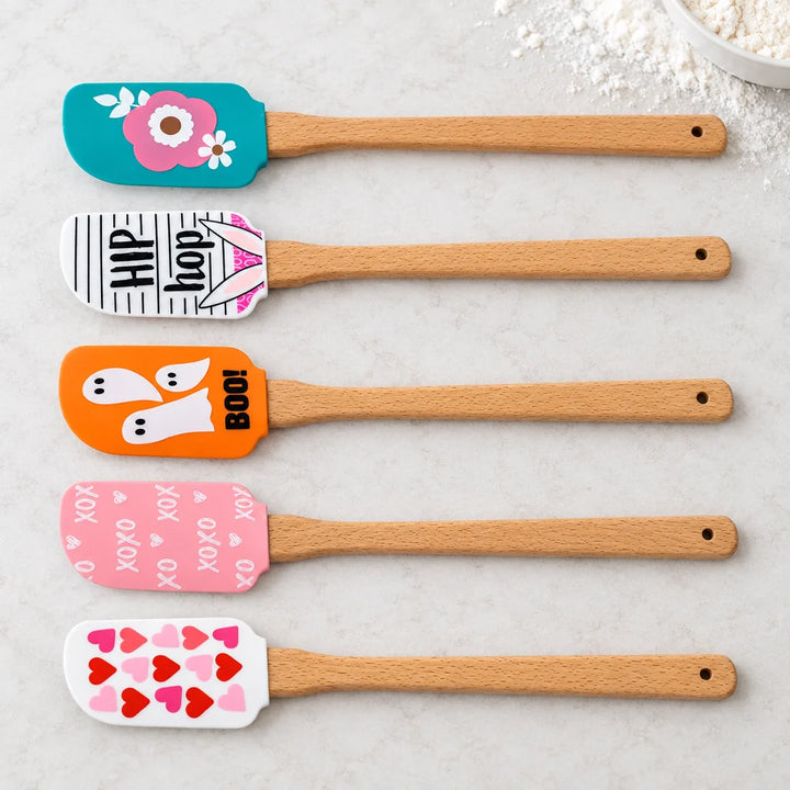 Five ice cream style silicone baking spoons with wooden handles laid in a row, top view