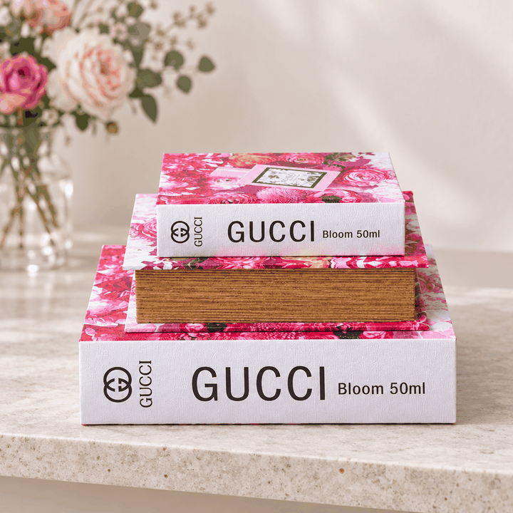 Three pink floral book decor boxes stacked flat beside vase of roses, spine view