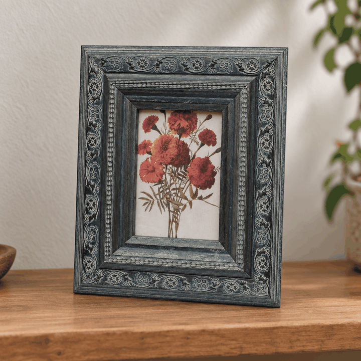 Grey ornate carved photo frame with red floral print on wooden table
