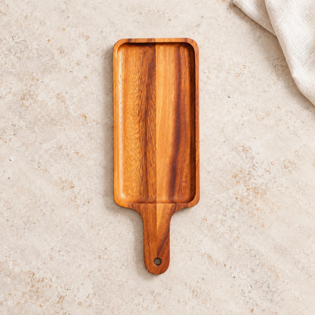 Single long wooden serving platter with handle and hanging hole on a neutral stone tabletop