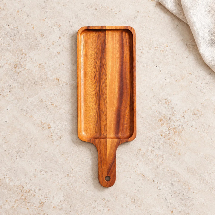 Single long wooden serving platter with handle and hanging hole on a neutral stone tabletop