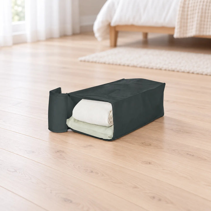 Black Garmento storage bag with open end flap and folded bedding in a bedroom setting