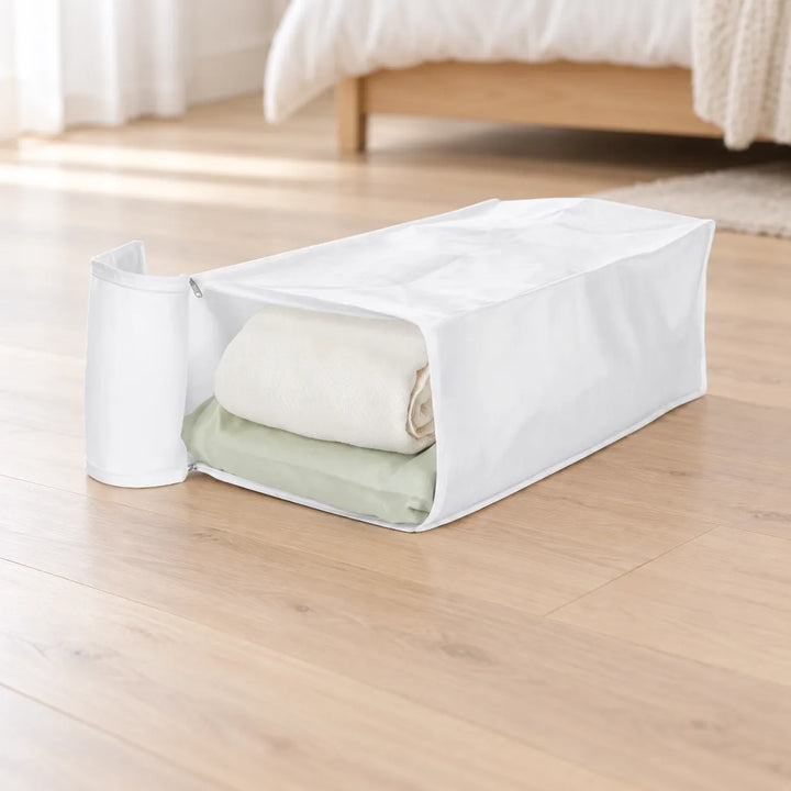 White Garmento storage bag with open end flap and folded bedding in a bedroom setting