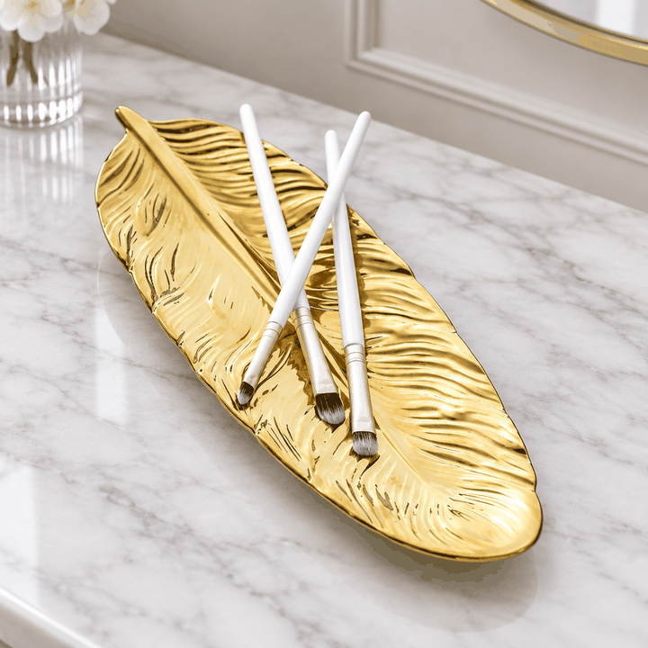 Gold feather shaped jewellery plate holding two pens on white marble desk