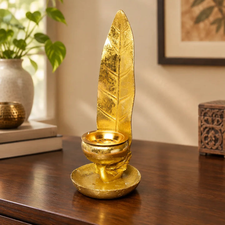 Gold leaf candle holder on wooden sideboard beside books and a potted plant