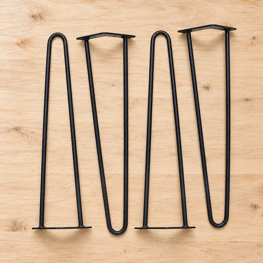 Pack of four matte black two-rod hairpin table legs with mounting plates on a pale wooden workbench; size selected separately.