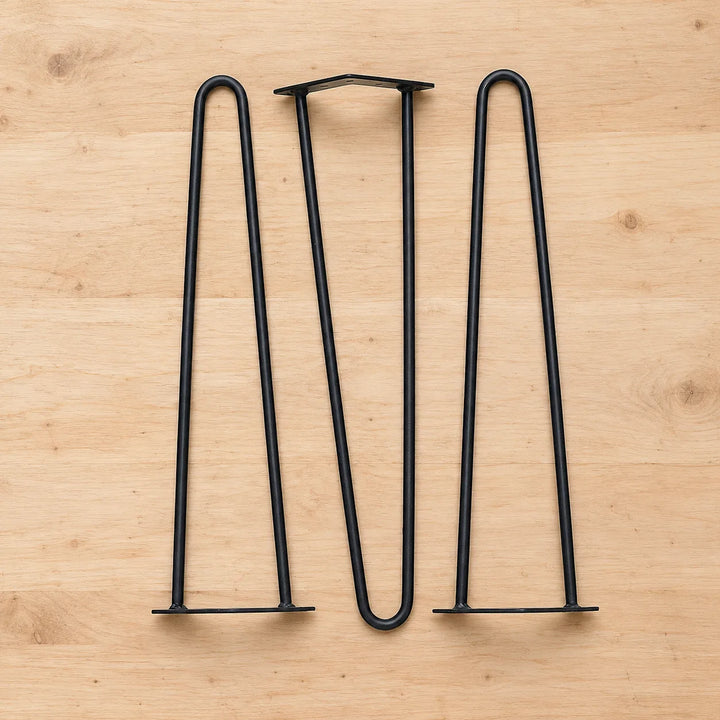 Pack of three matte black two-rod hairpin table legs with mounting plates on a pale wooden workbench; size selected separately.