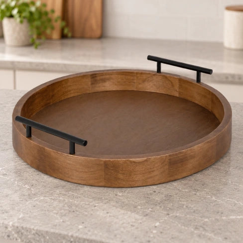 Empty round brown wooden serving tray with black bar handles on a neutral kitchen counter