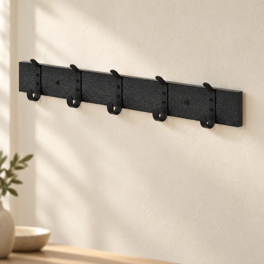 Black five-double-hook wall coat rack shown mounted in a softly lit hallway; original wood grain and hardware retained