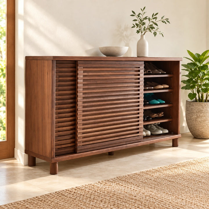 Walnut brown wide shoe cabinet with slatted sliding door partly open in a warm sunlit entryway