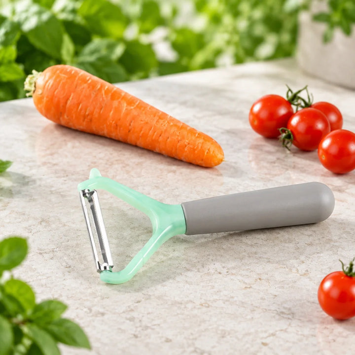Mint green and grey vegetable peeler beside peeled carrot and cherry tomatoes on counter