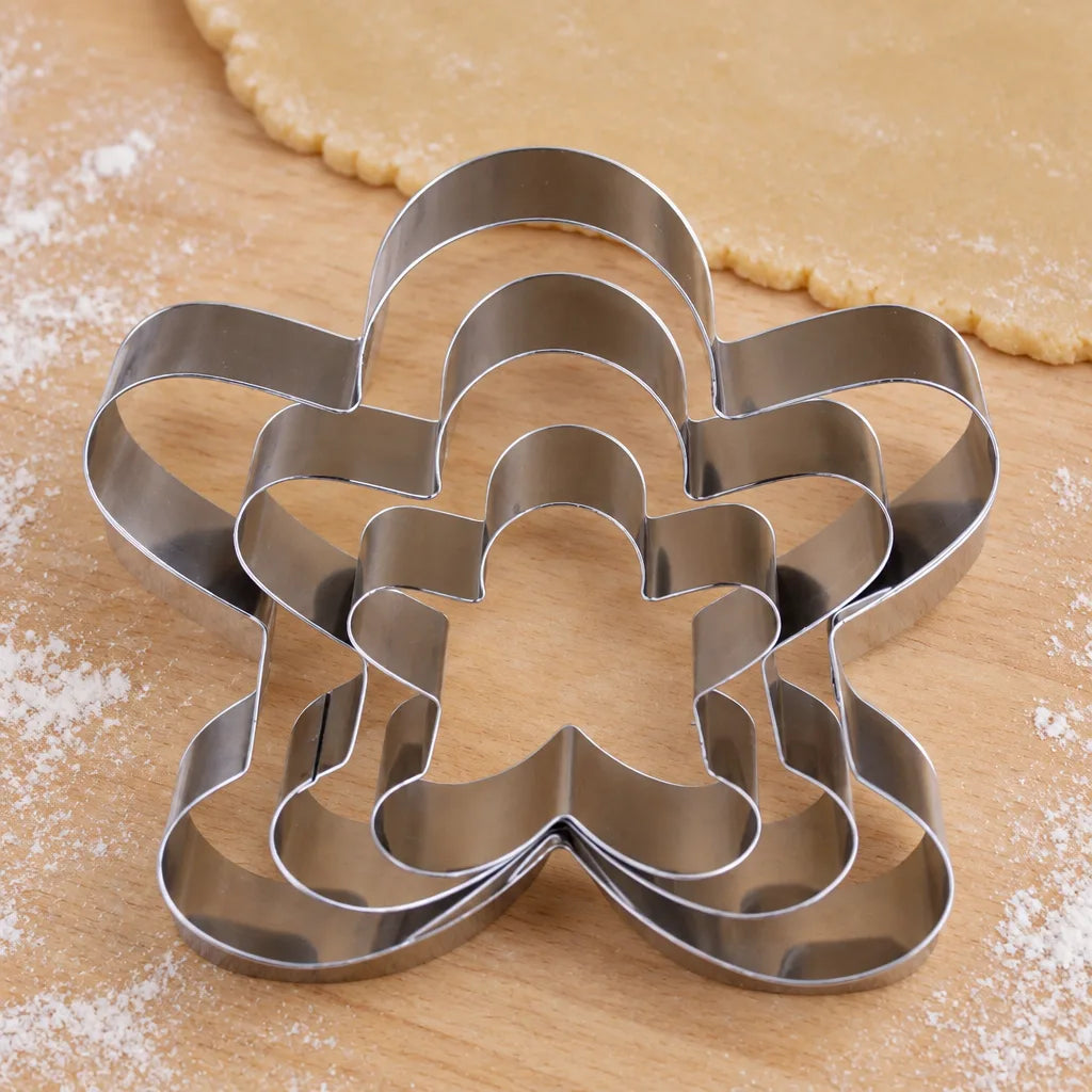 Three nested steel cake and cookie baking moulds in flower, star and gingerbread shapes on dough