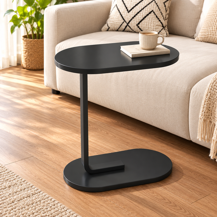 Black oval side table with C-shaped support beside a sofa in a sunlit living room