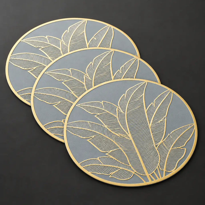Three round grey and gold leaf pattern table mats on dark surface