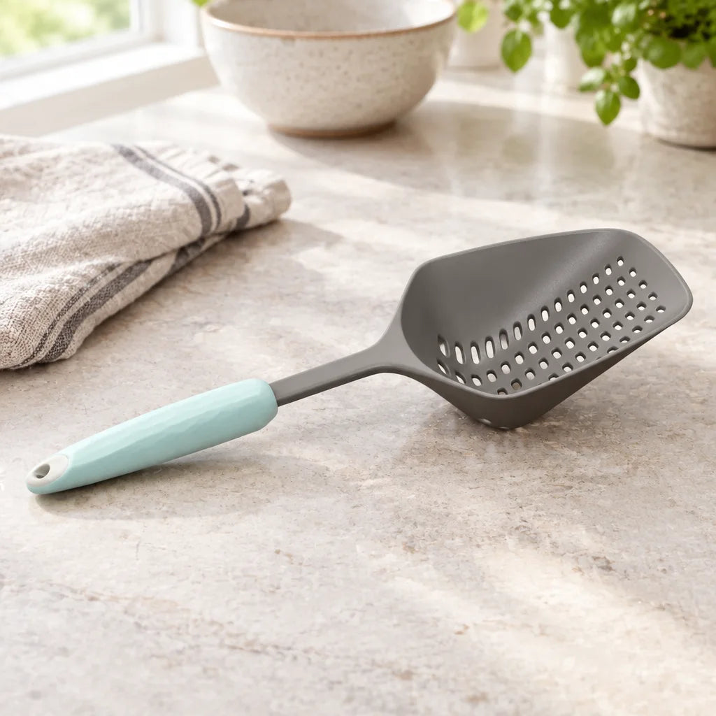 Grey spoon colander with mint handle on marble kitchen counter beside folded towel