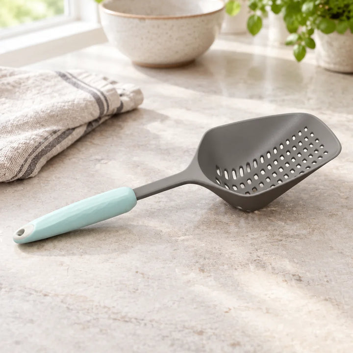 Grey spoon colander with mint handle on marble kitchen counter beside folded towel