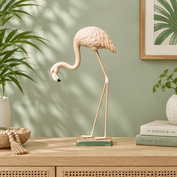Light pink flamingo statue decor with gold legs on sideboard against green wall