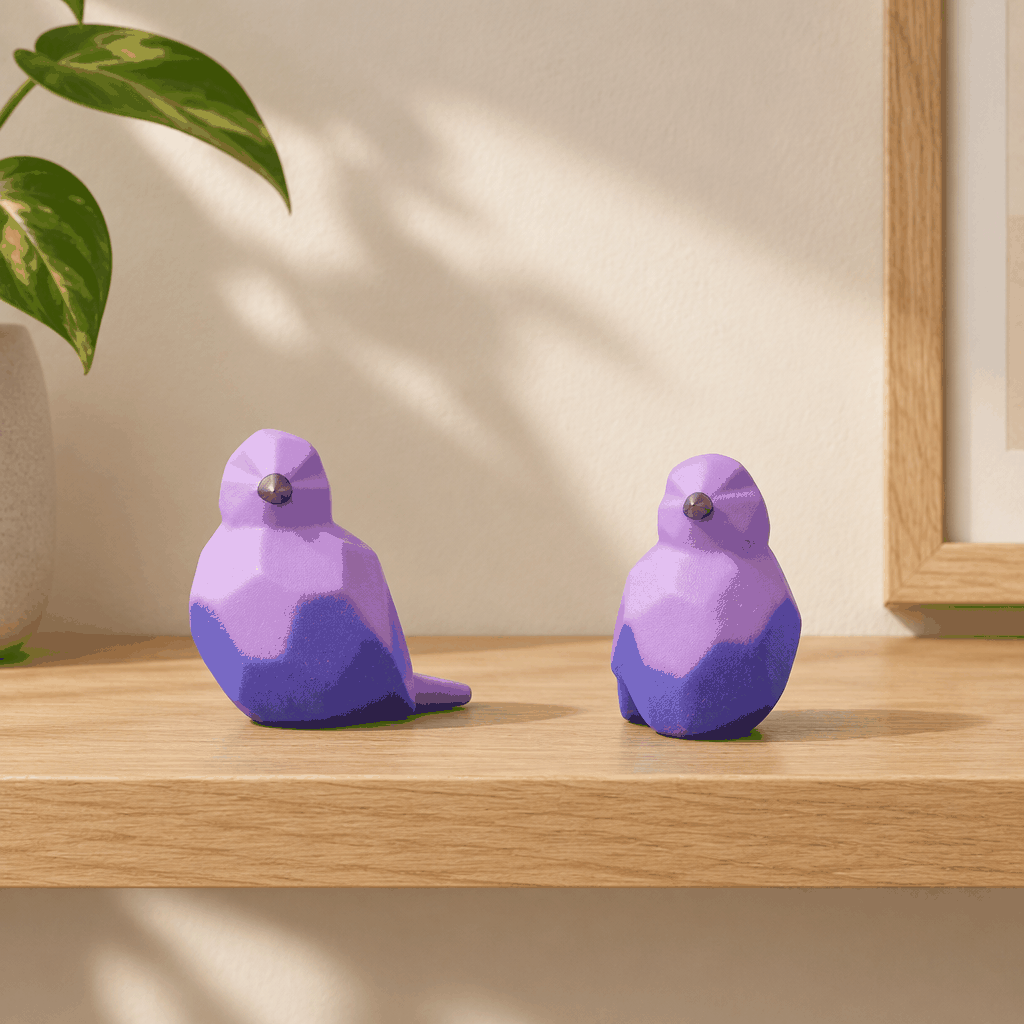 Pair of purple geometric bird decor figurines on wooden shelf with leafy plant