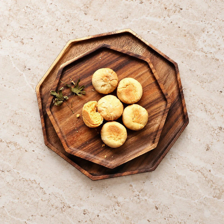 Set of two stacked octagon wooden serving trays styled with pastries on a light stone tabletop