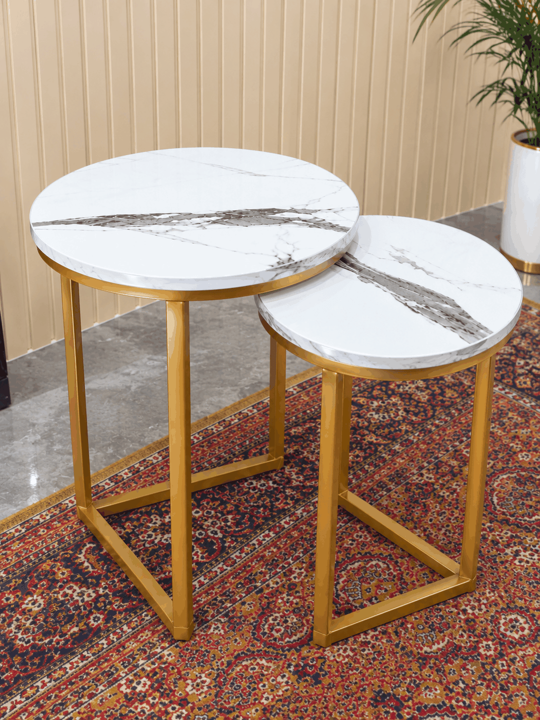 Two round white marble nesting tables with gold legs on red patterned rug