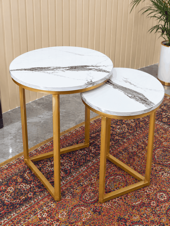 Two round white marble nesting tables with gold legs on red patterned rug