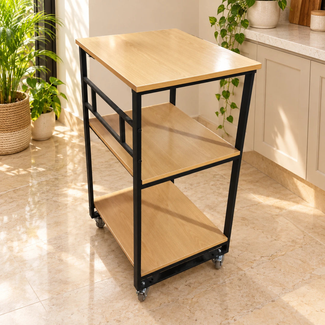 Rollout trolley with three flat light wood laminate shelves, black frame and casters in a sunlit kitchen