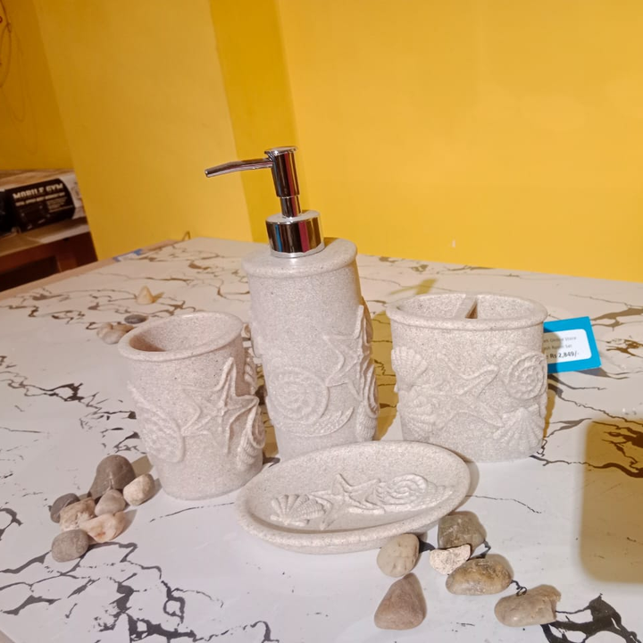 Beige embossed ceramic bathroom set with soap dispenser, two tumblers and soap dish on marble table