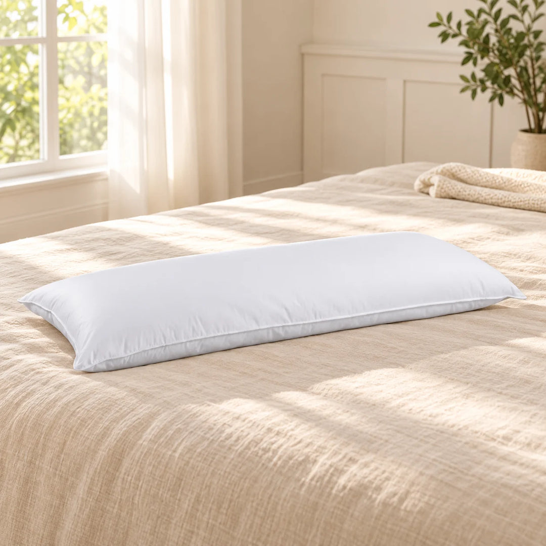 Single long white body pillow with piped seam on beige bedding in a calm natural-light bedroom