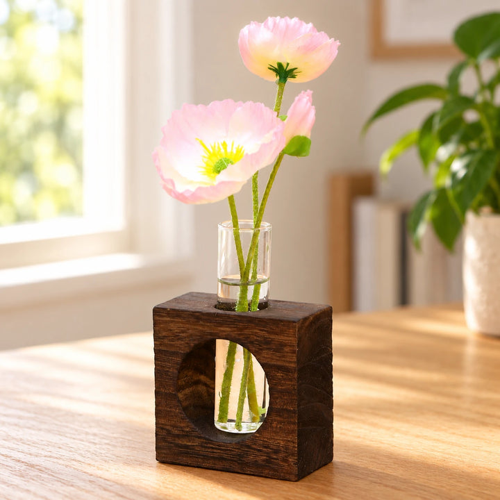 Dark wooden block and glass test-tube vase with pink flowers in natural window light