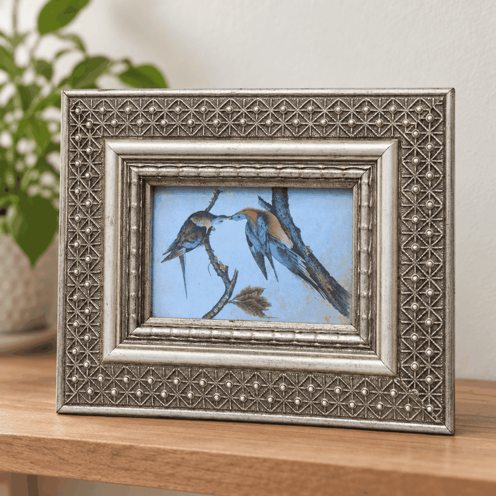 Silver beaded rectangular photo frame with bird artwork on wooden table