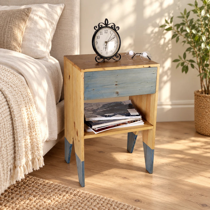 Side table with a blue-gray front and dipped legs beside a bed