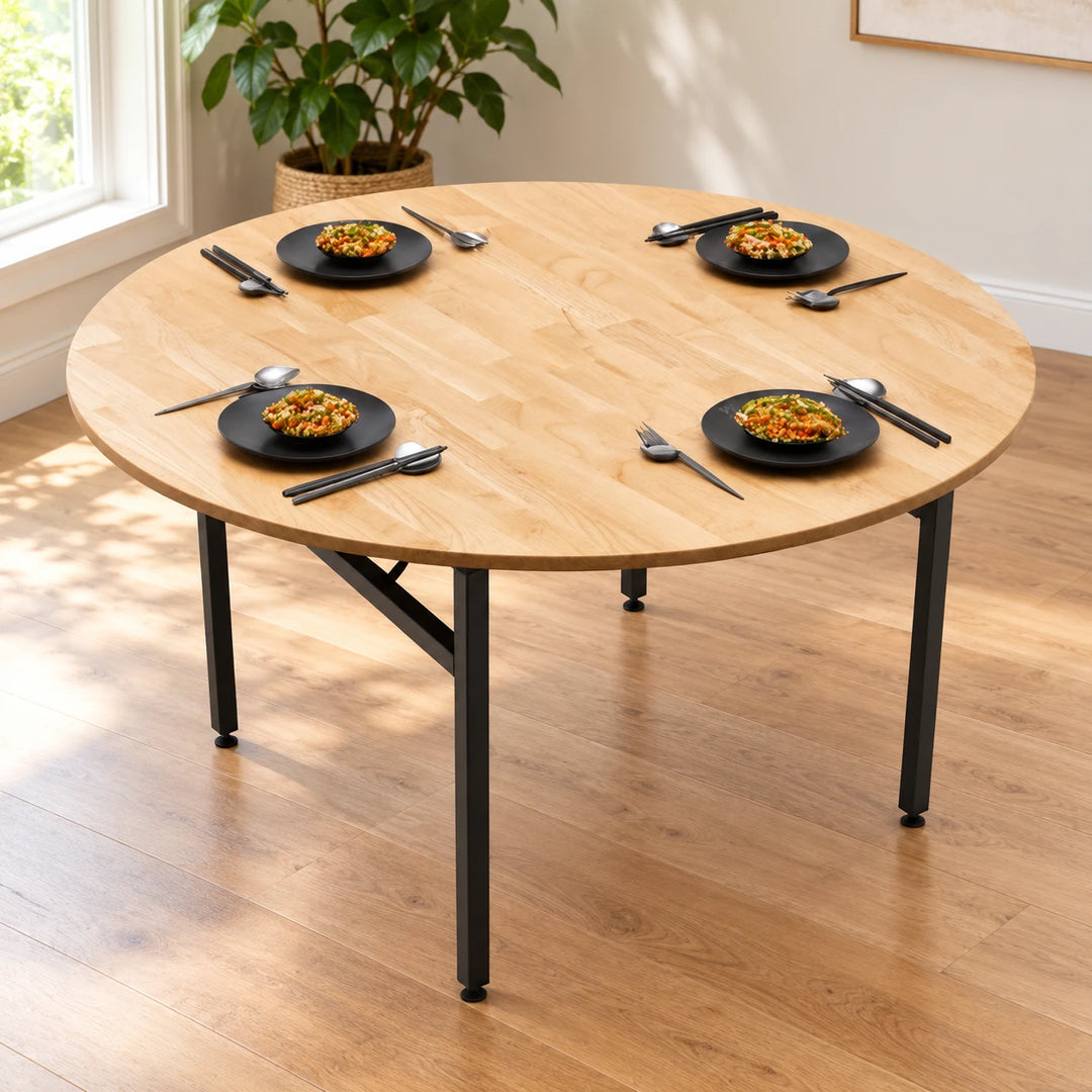 Round light wood dining table with four black legs and four place settings in a sunlit dining room